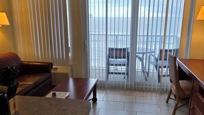 A hotel room with a large bed, a sofa, a dining table, and a view of the sea through a sliding door. - Relaxing Oceanfront 7th floor Condo 2-bath, sleeps  up to 4 (Daytona Beach)
