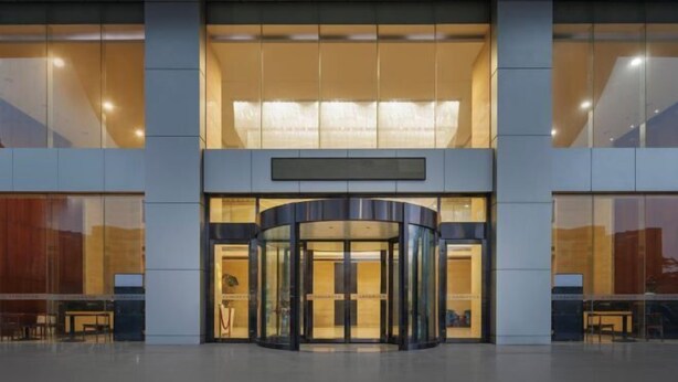 Una entrada moderna de edificio con puerta giratoria y grandes ventanales.