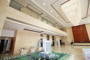 A spacious lobby with a high ceiling, a model building, and a glass railing. - Wenhai International Hotel (Qingdao)