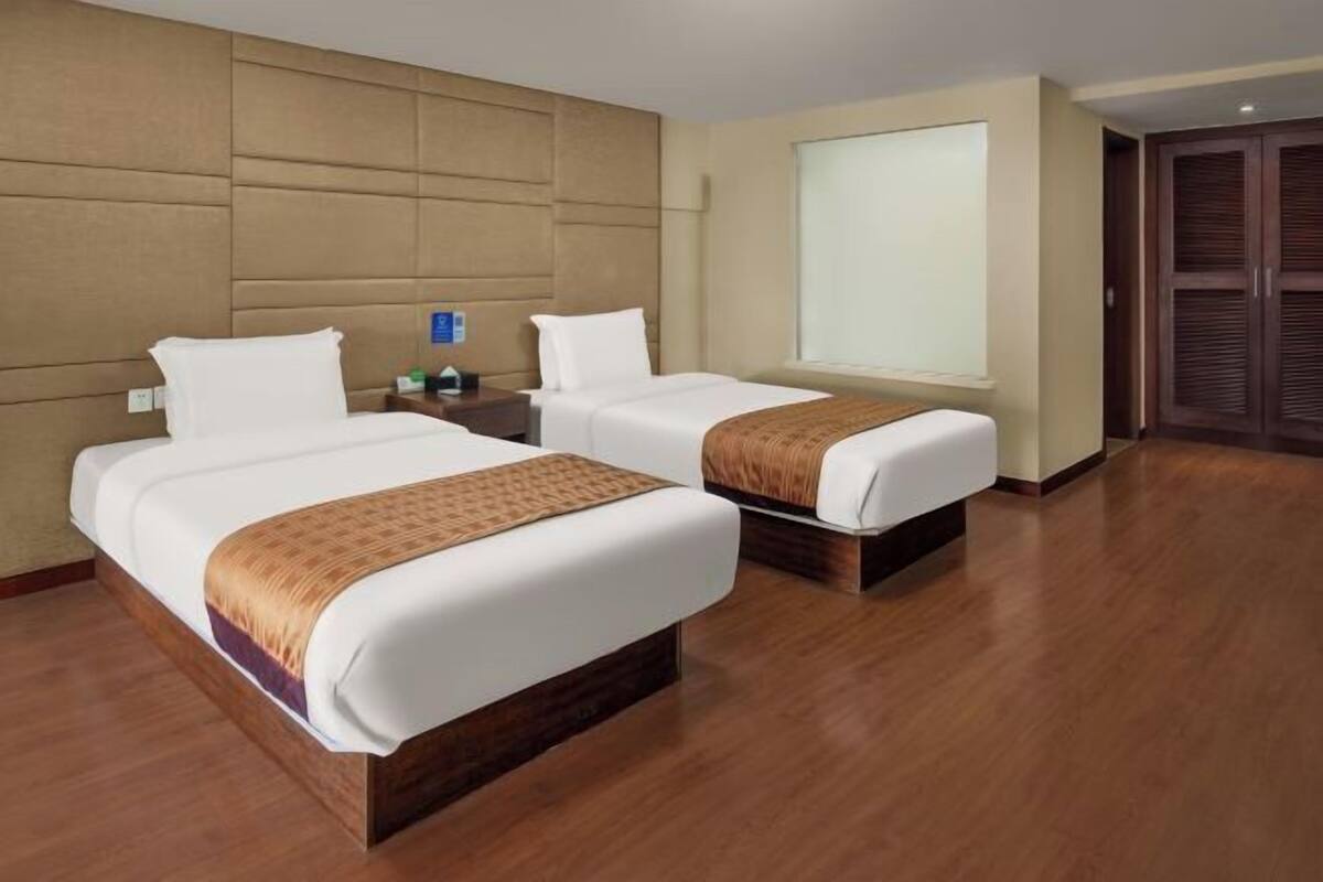 A hotel room with two beds, a large window, and a wooden floor.