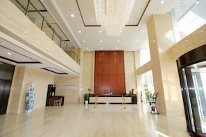Um hall amplo com teto alto, balcão de recepção e um grande painel de parede de madeira.