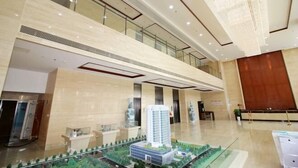 Un moderno vestíbulo de hotel con barandilla de cristal, una maqueta de edificio y una lámpara de araña.