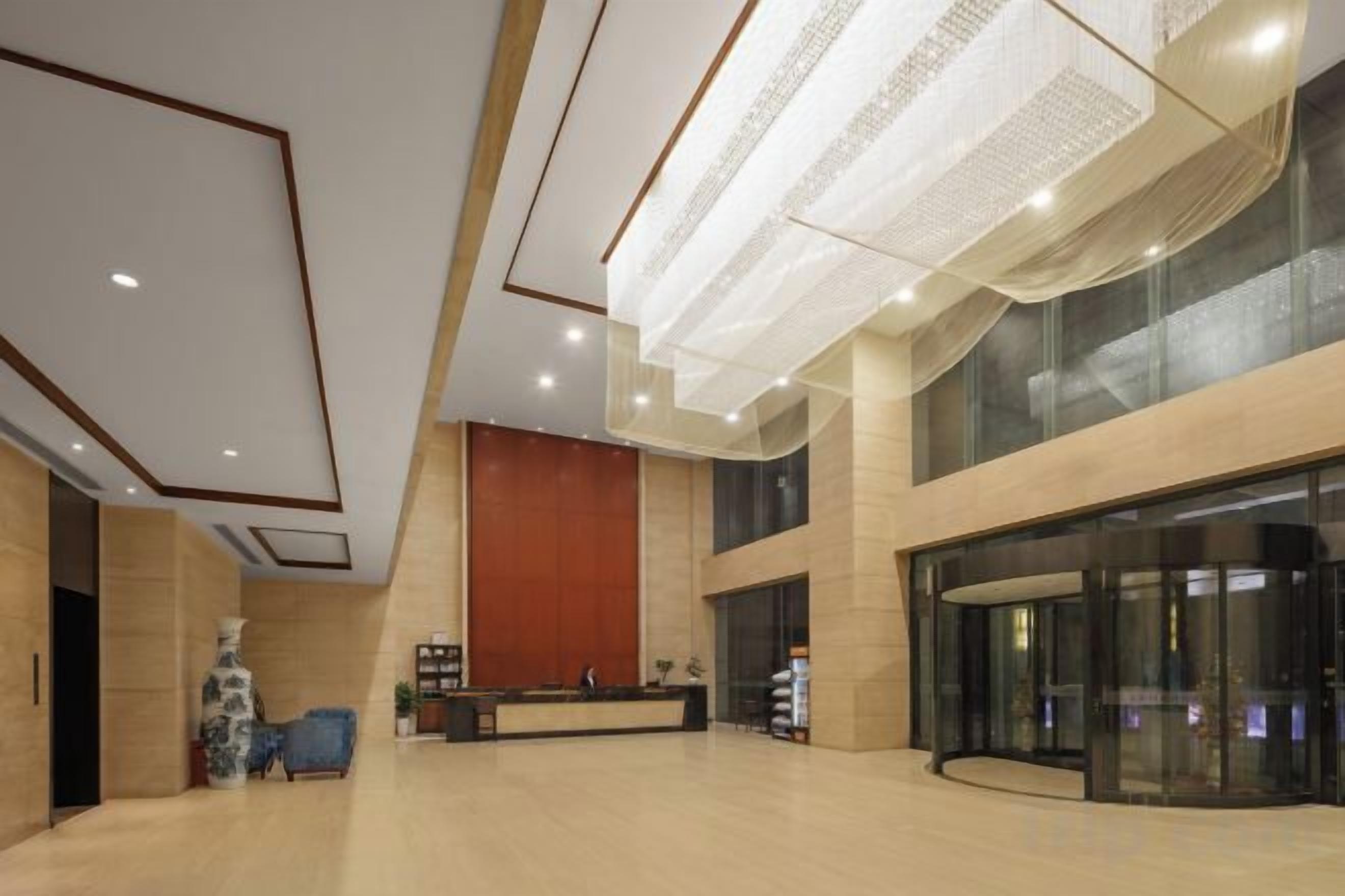 A spacious lobby with a reception desk, a large wooden panel wall, and a glass elevator entrance.