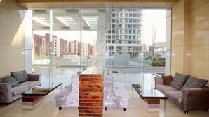 Un moderno vestíbulo de hotel con un separador de vidrio, dos sofás, una mesa de centro y una estructura decorativa de madera.