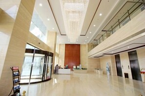 A spacious lobby with a reception desk, a large chandelier, and a glass elevator.