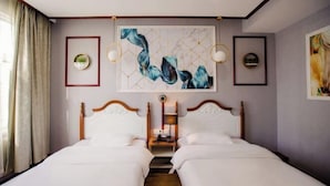 Une chambre d’hôtel avec deux lits, une table de chevet, une lampe fixée au mur et des œuvres d’art.