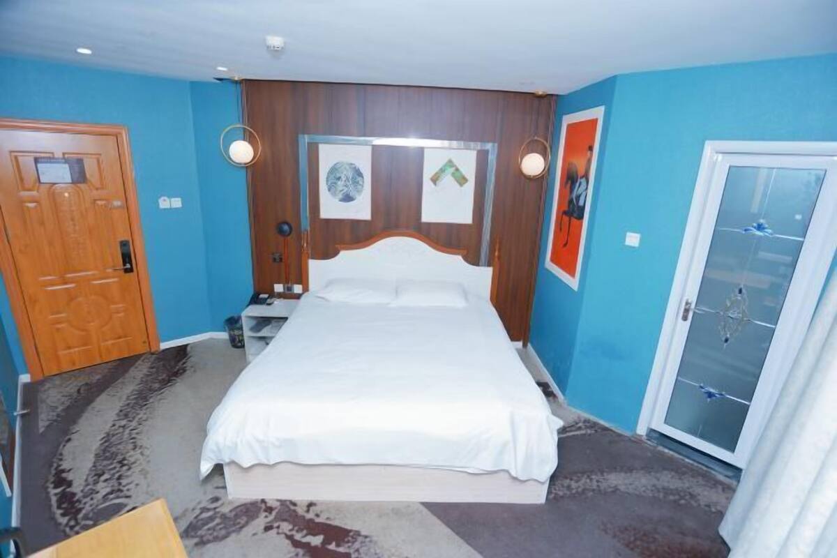 Ein Schlafzimmer mit einem Bett, einer Holztür, einer Wandleuchte und einer Tür mit Fensterteil.