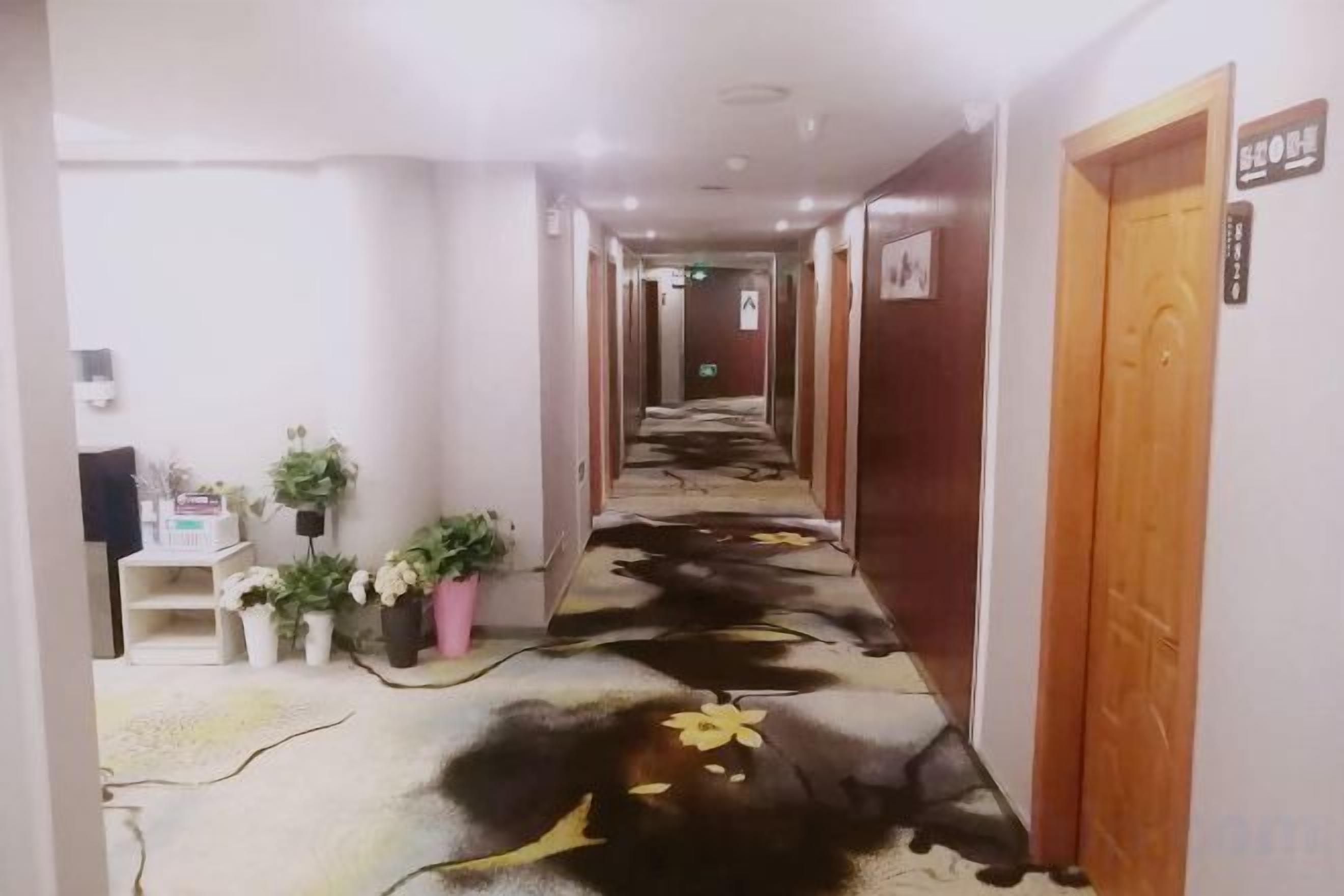A hotel hallway with a carpeted floor, wooden doors, and potted plants.