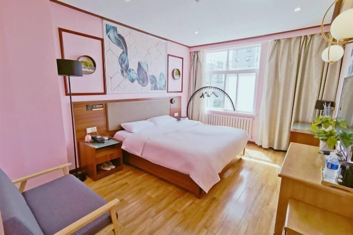 Ein Hotelzimmer mit Bett, Nachttisch, Lampe und einem Fenster mit Vorhängen.