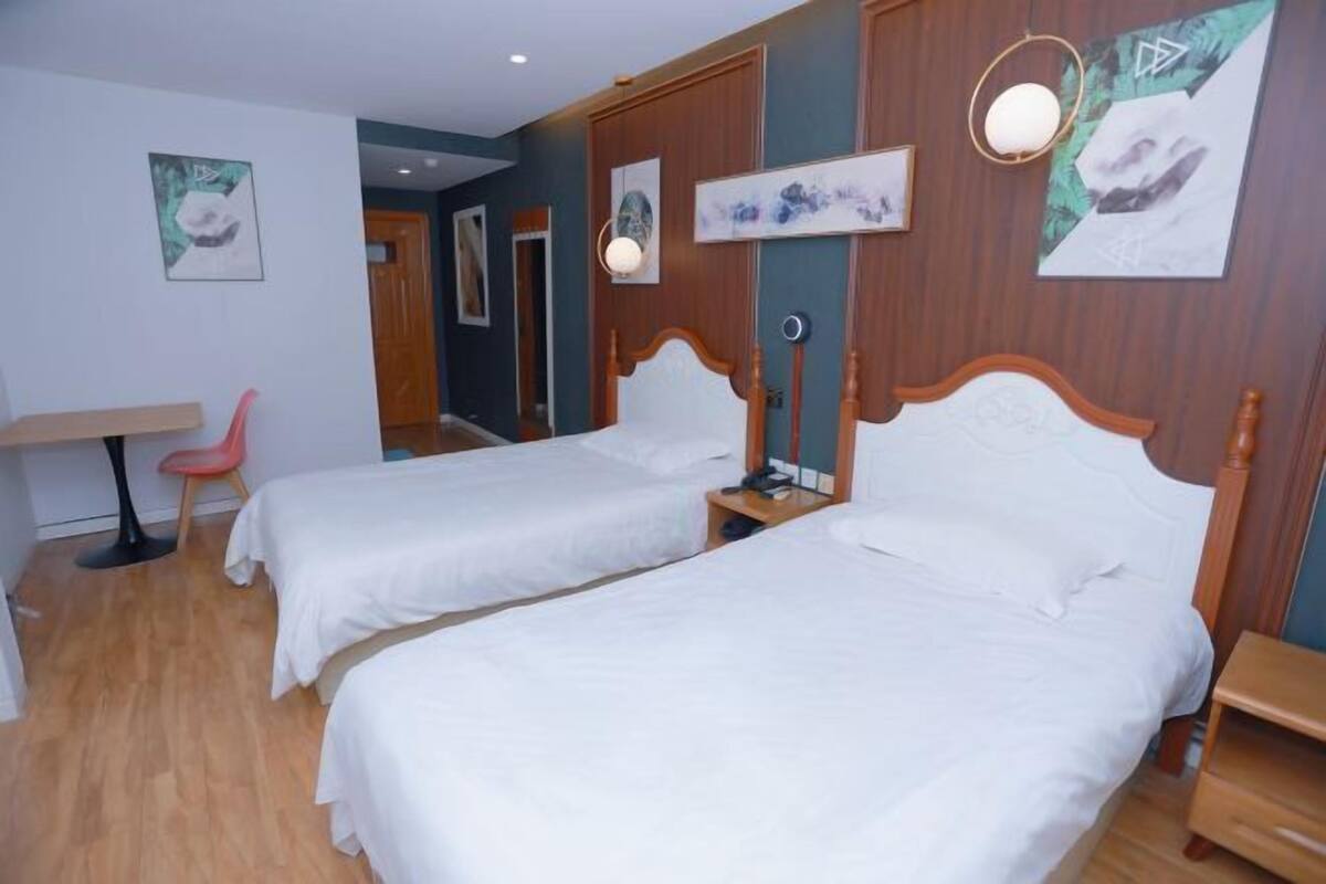 Ein Hotelzimmer mit zwei Betten, einem Schreibtisch, einem Stuhl und Bildern an den Wänden.