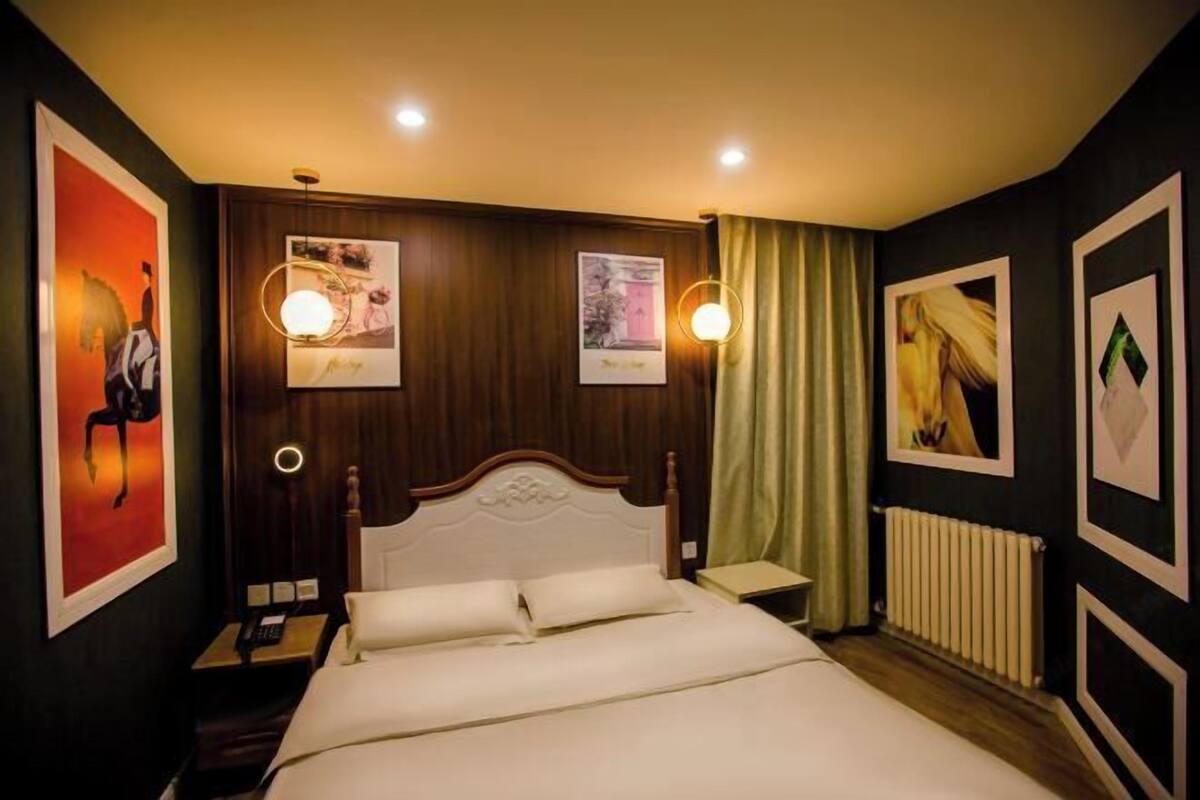 Ein Hotelzimmer mit einem Bett, einem Nachttisch, einer Lampe und gerahmten Bildern an den Wänden.