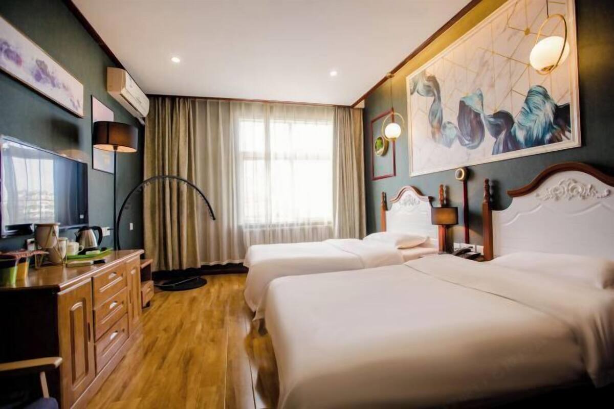 Ein Hotelzimmer mit zwei Betten, einem Schreibtisch, einem Fernseher, einer Lampe und Kunstwerken an den Wänden.