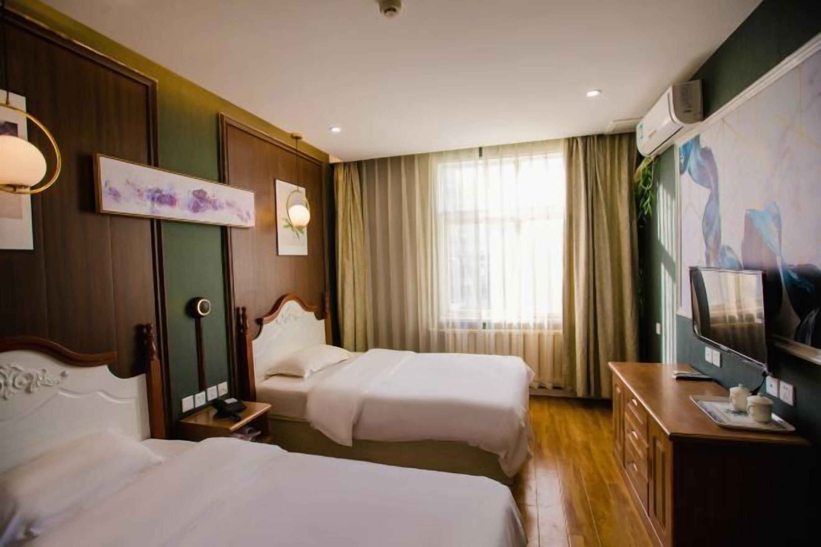 Quarto de hotel com duas camas, televisão, escrivaninha e janela com cortinas.