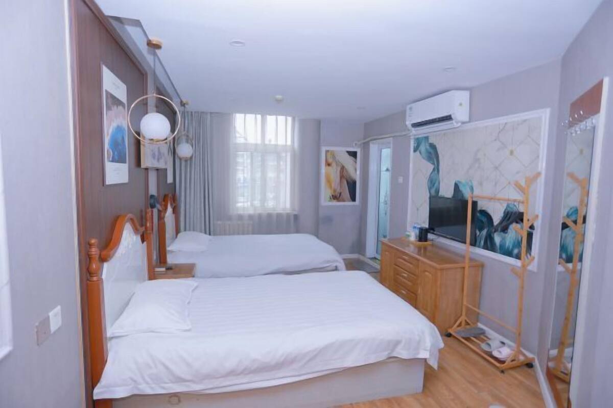 Ein Hotelzimmer mit zwei Betten, einem Holzkoffer, einem Spiegel und einem Gemälde an der Wand.