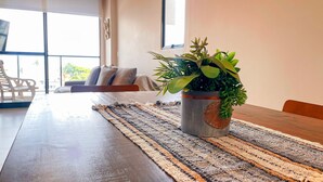 A dining area with a long table, a woven placemat, and a potted plant. - Flat Oceânica Frente Mar - By Almare (Joao Pessoa)