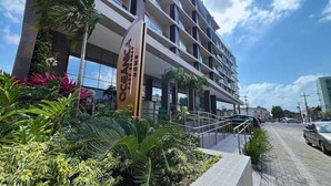 A modern hotel with a prominent sign, a well-maintained garden, and a clear sky. - Flat Oceânica Frente Mar - By Almare (Joao Pessoa)