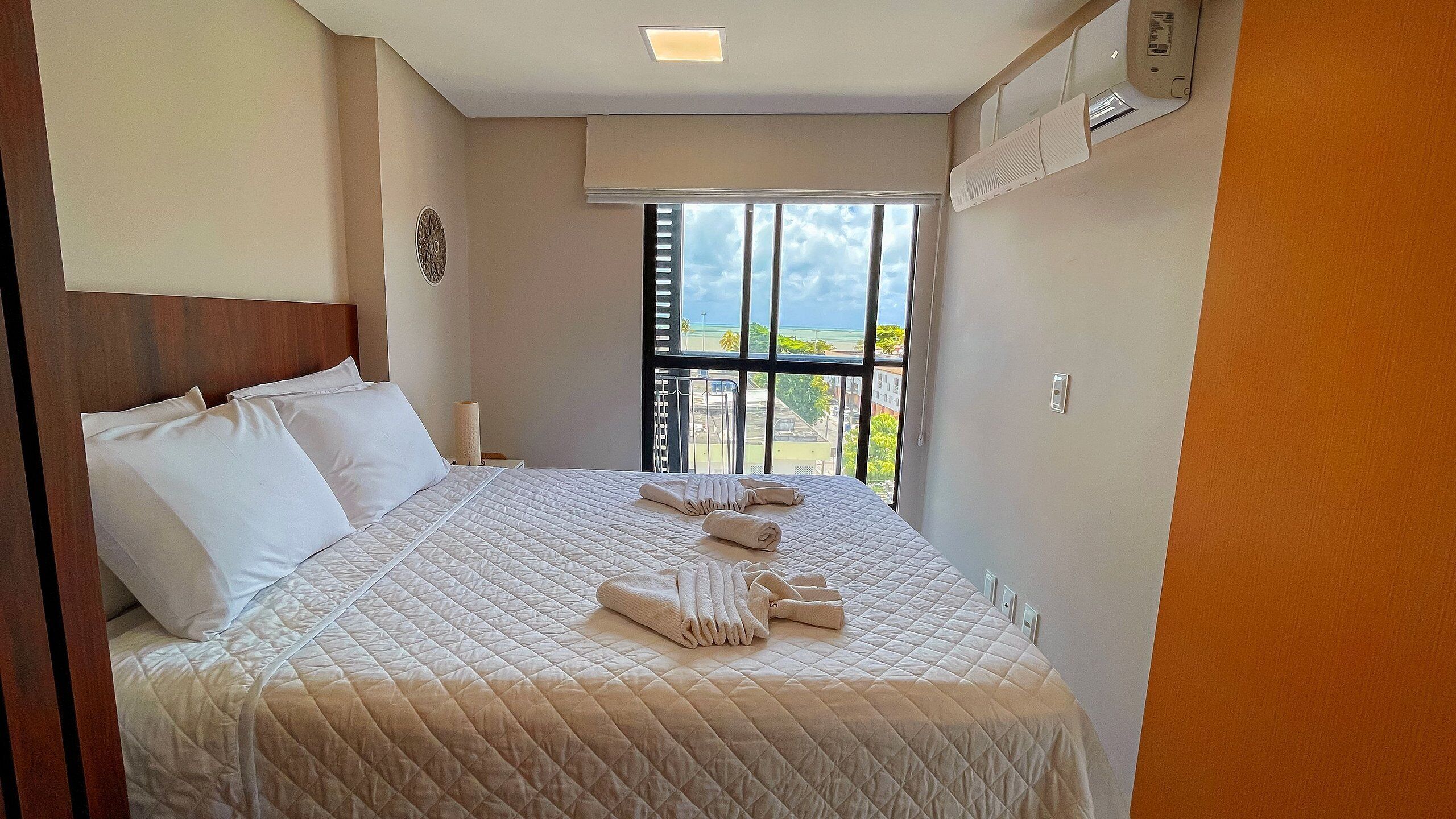 A hotel room with a large bed, a window with a view of the beach, and a ceiling fan.