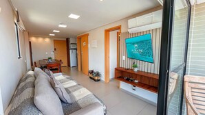 A modern living room with a sofa, TV, and a dining area. - Flat Oceânica Frente Mar - By Almare (Joao Pessoa)