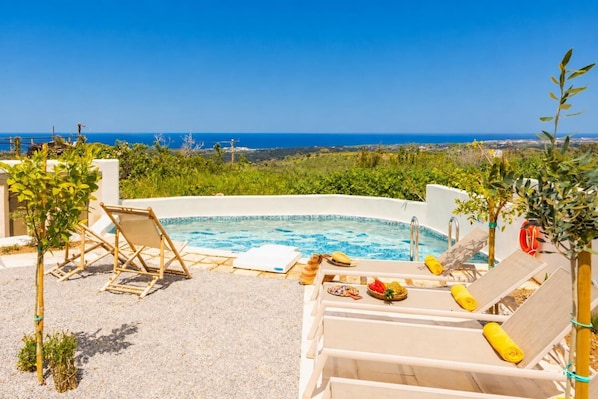 Un bain à remous avec vue sur la mer, entouré de chaises longues et de petites plantes.