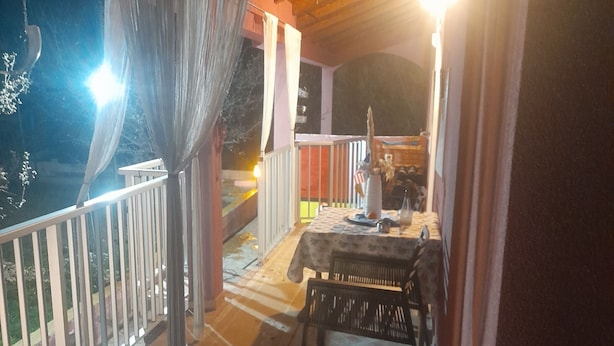 A balcony with a table and chairs, a railing, and a view of the street at night. - Holiday Home Village Paradise - Holiday Home (Zemunik)