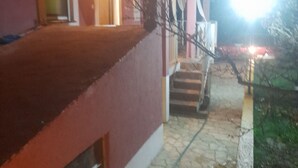 A building with a red facade, a staircase leading to a porch, and a bright light source in the background. - Holiday Home Village Paradise - Holiday Home (Zemunik)