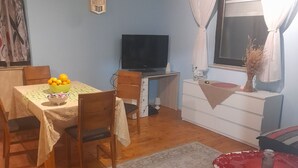 A dining area with a table set for two, a television, a white dresser, and a window with curtains. - Holiday Home Village Paradise - Holiday Home (Zemunik)