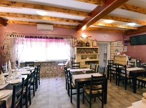 A cozy restaurant with wooden beams, stone walls, and a stone fireplace. Tables are set with white tablecloths and chairs. - Authentic Istrian Rooms for Unforgettable Stays - Triple Room (Vodnjan)