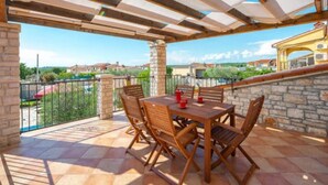 A covered patio with a table and chairs, stone walls, and a view of the surrounding area. - Holiday Home Luna - Holiday Home (Vodnjan)