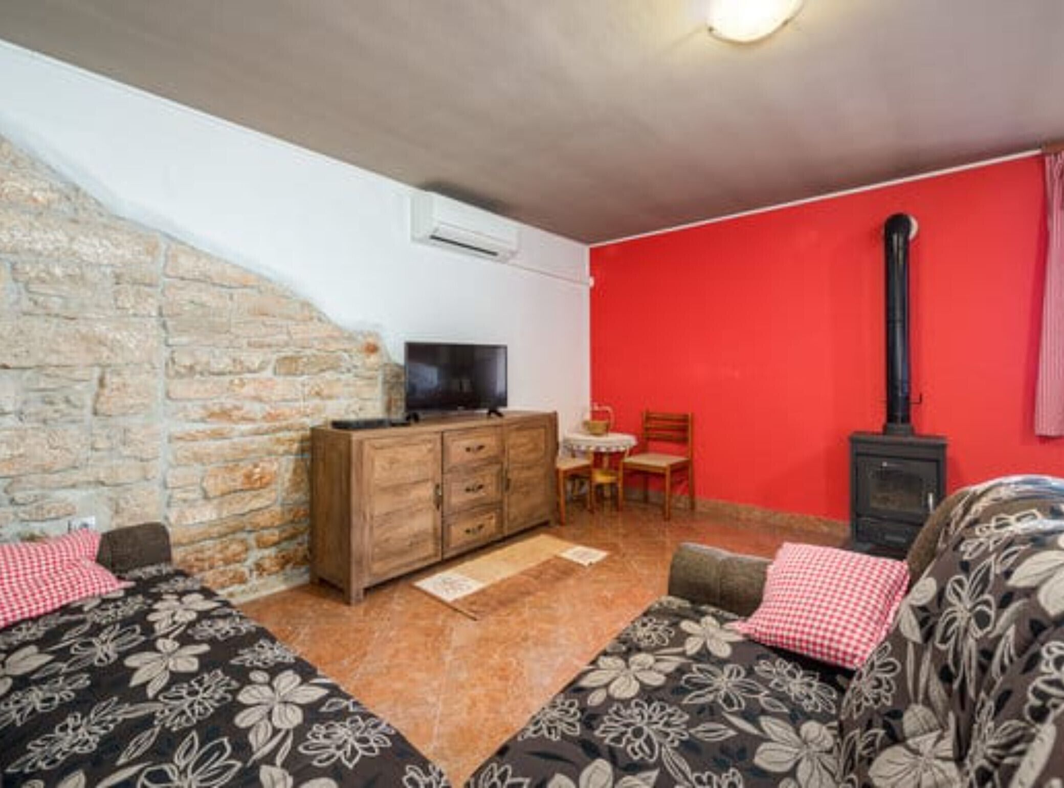 A cozy room with a stone wall, a wooden dresser, a television, a red wall, a fireplace, and two patterned sofas.