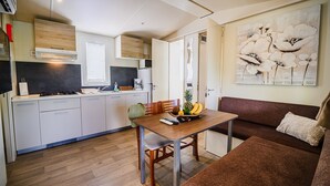 Un espacio habitable compacto con kitchenette, una mesa de comedor con frutero y un sofá con cojín.