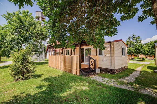 A small wooden cabin with a porch and a door, surrounded by trees and grass.