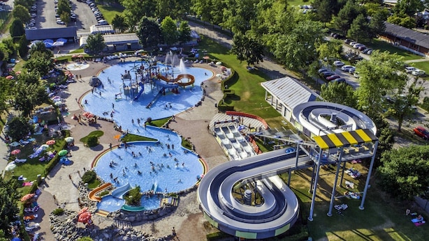 Une vue aérienne d’un parc aquatique avec de nombreux toboggans et piscines, entouré d’arbres et d’un parking.