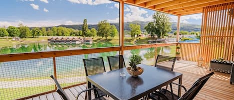 A covered outdoor area with a table and chairs, overlooking a lake and a golf course.