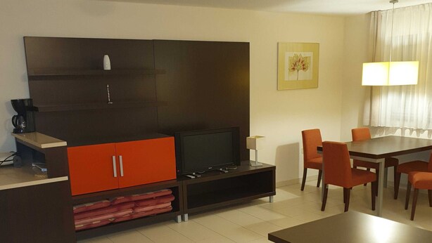 Una habitación de hotel moderna con sofá, una mesa de centro, televisor, mesa de comedor con sillas y un armario grande.