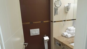 Un baño pequeño con inodoro, toallero con toallas, secador de pelo y dispensador de papel.