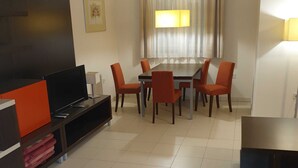 Una sala de estar moderna con un televisor de pantalla plana, una mesa de comedor con seis sillas y un ventanal con cortinas.