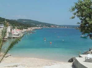 A coastal view with clear blue water, a sandy beach, and a small pier with umbrellas.