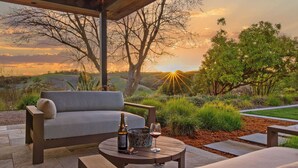 A patio with a sofa, a table, and a bottle of wine, overlooking a scenic landscape with trees and hills during sunset. - Wine Country Estate w/ Pool, Hot Tub The Residence at Truss Wines by Avantstay (Paso Robles)