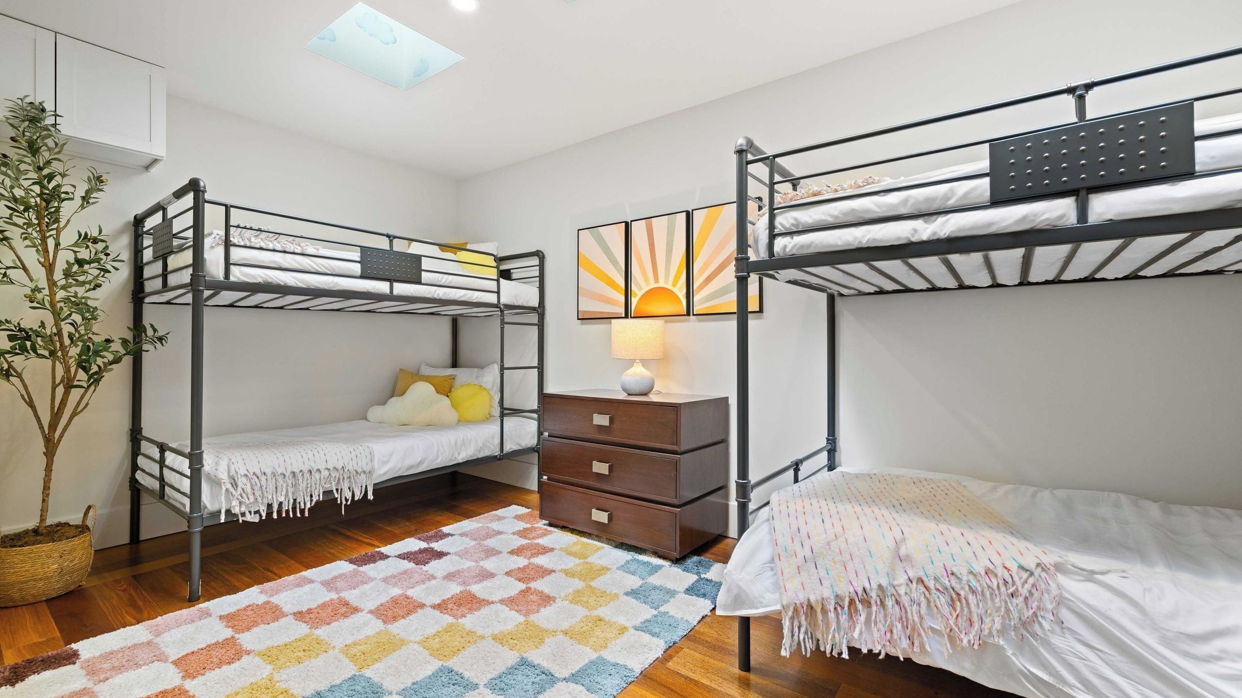 A bunk bed room with a ceiling fan, a small table with a lamp, and a colorful rug.