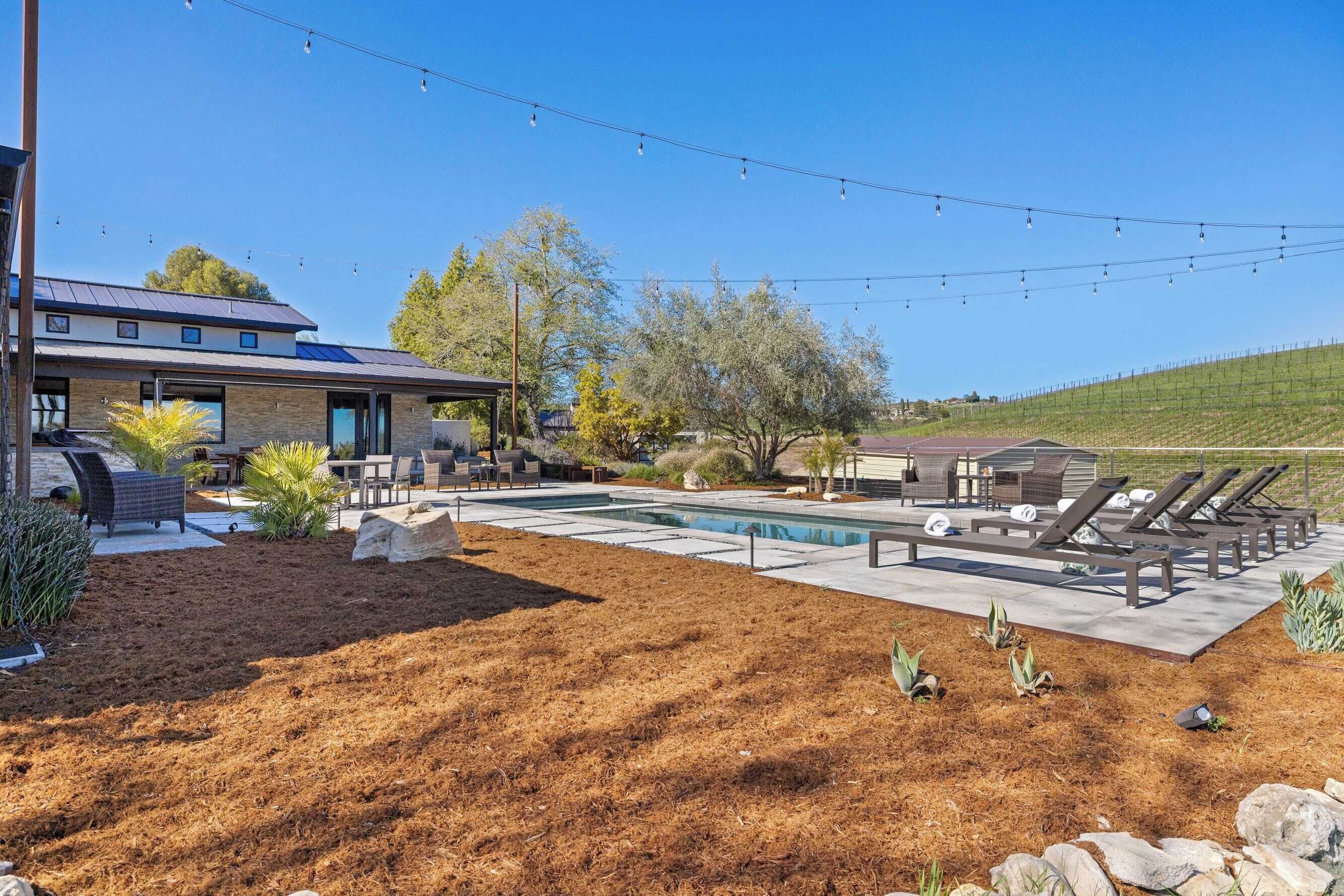 A modern outdoor pool area with lounge chairs, a barbecue area, and a stone pathway.