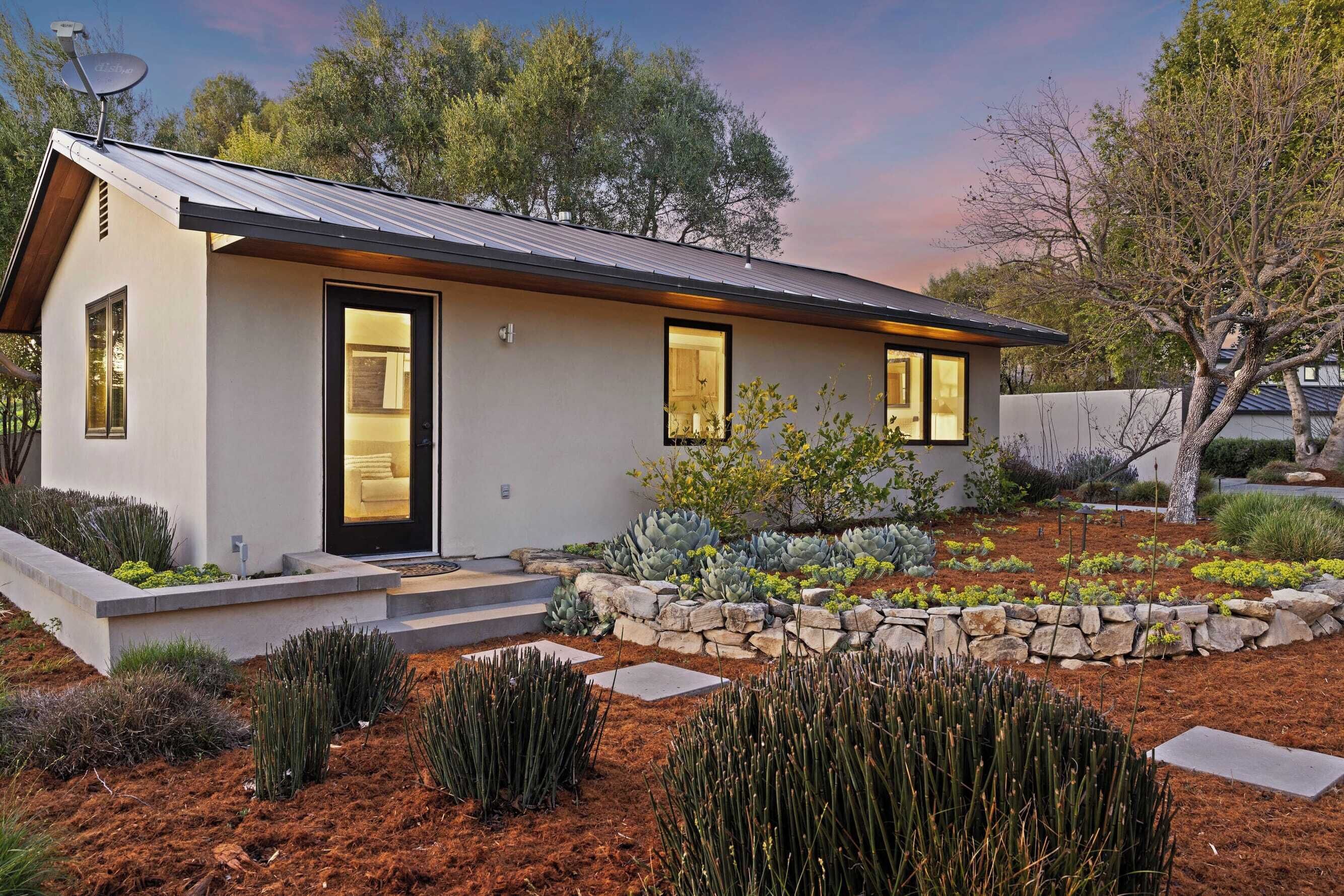 A modern house with a flat roof, a stone pathway, and a garden with various plants.