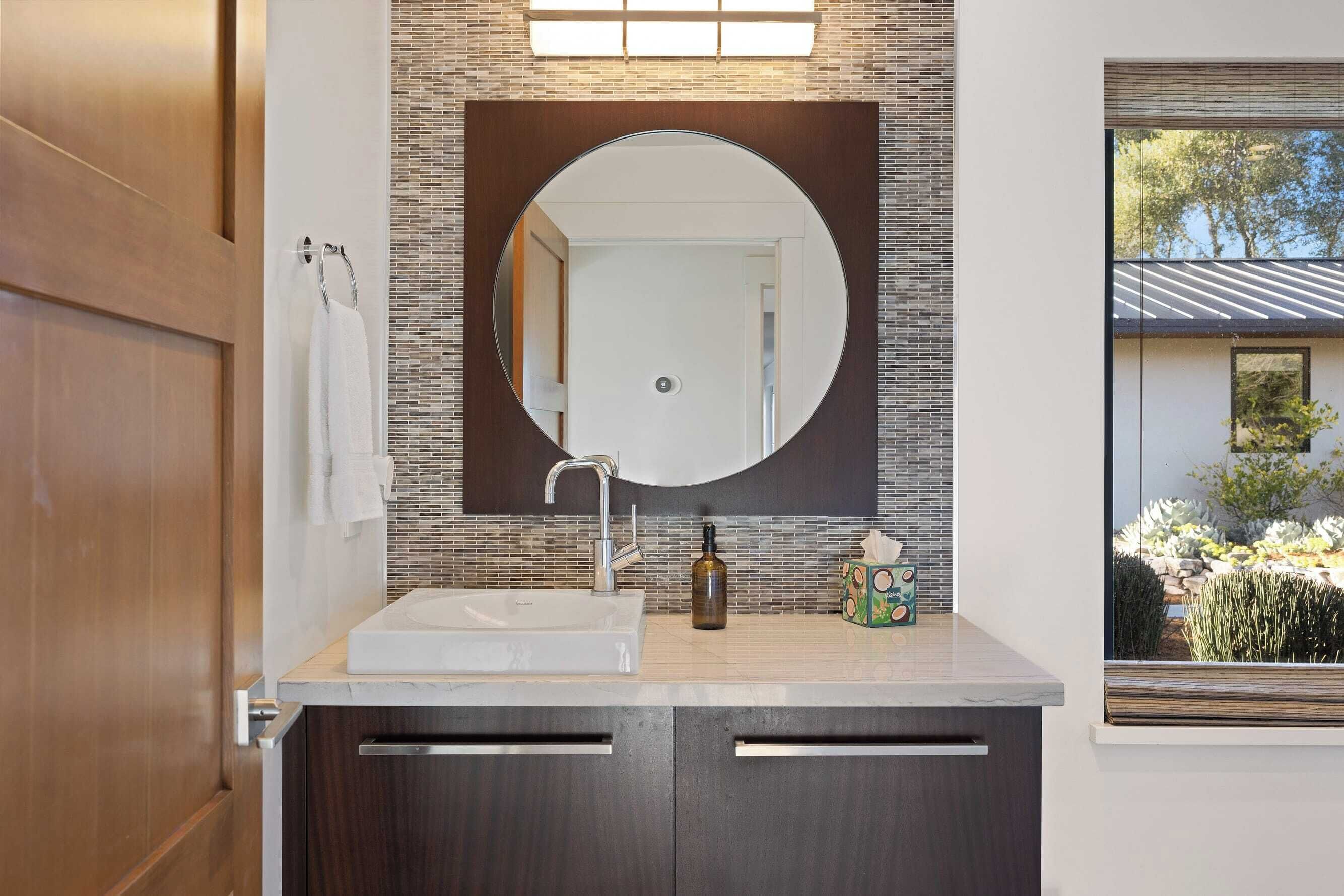 A modern bathroom with a large mirror, a sink, and a window providing a view of the outdoors.