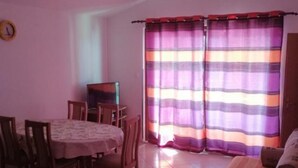 A dining area with a table and chairs, a television on a stand, and a window with striped curtains.