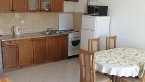 A small kitchen with wooden cabinets, a microwave, a stove, and a sink. There is a dining table with chairs.