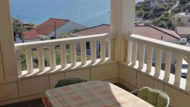 A balcony with a table and chairs, overlooking a coastal area with houses and the sea.