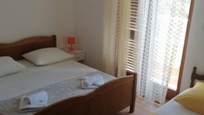 A bedroom with a wooden bed, white bedding, a nightstand with a lamp, and sheer curtains.