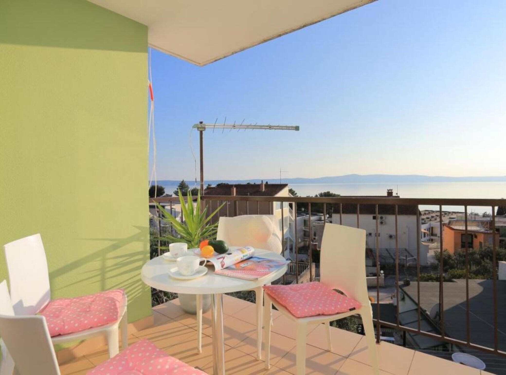 Un balcon avec une table et des chaises, un pot de fleurs et une vue sur une étendue d’eau et des montagnes lointaines.