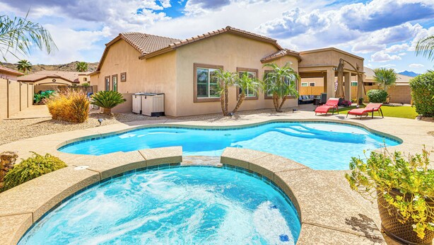 A swimming pool with a curved design, surrounded by a patio area with lounge chairs and palm trees.