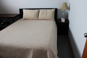 Un letto rifatto con cura, una coperta testurizzata, un comodino con una lampada e una sedia.