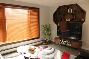 Una sala de estar con un ventanal grande, un televisor de pantalla plana, un mueble de entretenimiento de madera y una zona de comedor con mesa y sillas.